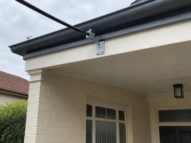 Overhead service cable and metal attachment bracket on a cream brick house fascia in Ryde